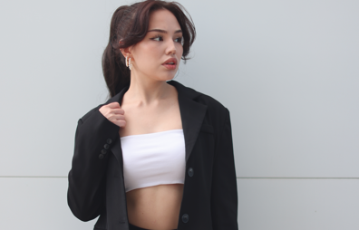 一位女性穿著黑色西裝外套和白色平口上衣，留著高馬尾，側身看著遠方