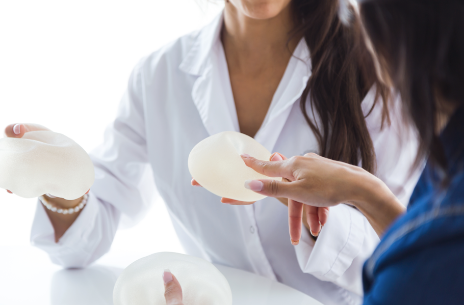 一位穿著白袍的人士正在向一位顧客展示並解釋兩個乳房植入物，顧客的手正指著其中一個