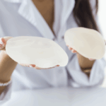 一位穿著白袍和珍珠手鍊的人，雙手各展示一個光滑的乳房植入物