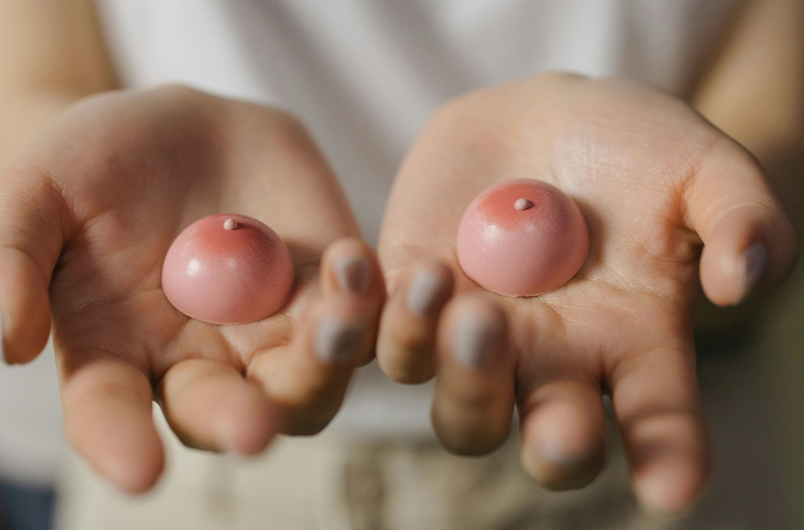 一雙手掌攤開，各放置一個粉紅色半圓形、帶有小尖端的乳頭形狀，象徵性的方式提及乳房需注意事項