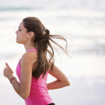 一名綁著馬尾的女性穿著桃紅色運動背心，在海灘上慢跑的側面影像