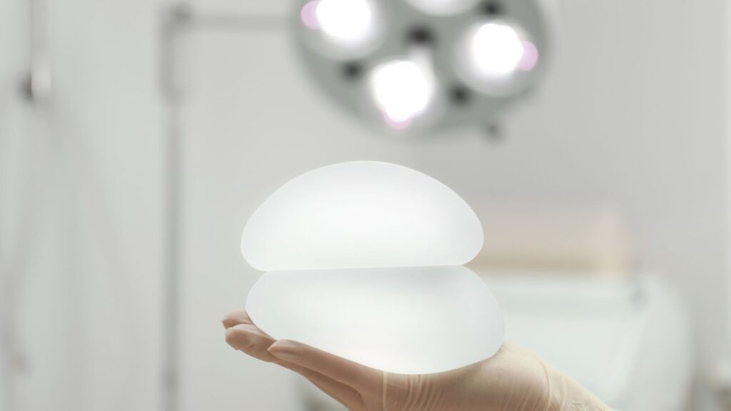 醫護人員手持兩顆圓盤型矽膠義乳展示其透明度與柔軟質感，背景為模糊的手術燈