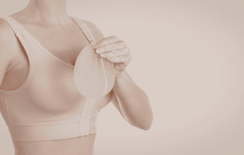 一名穿著膚色運動內衣或術後壓力衣的女性，手中拿著一個半透明的矽膠乳房植體。畫面呈現乾淨且專業的色調，常用於說明隆乳手術、乳房重建或義乳選擇等醫學美容與健康護理情境。