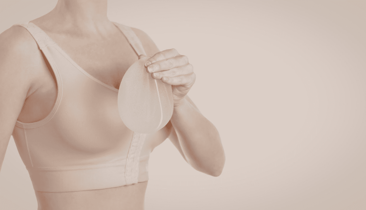 一名穿著膚色運動內衣或術後壓力衣的女性，手中拿著一個半透明的矽膠乳房植體。畫面呈現乾淨且專業的色調，常用於說明隆乳手術、乳房重建或義乳選擇等醫學美容與健康護理情境。