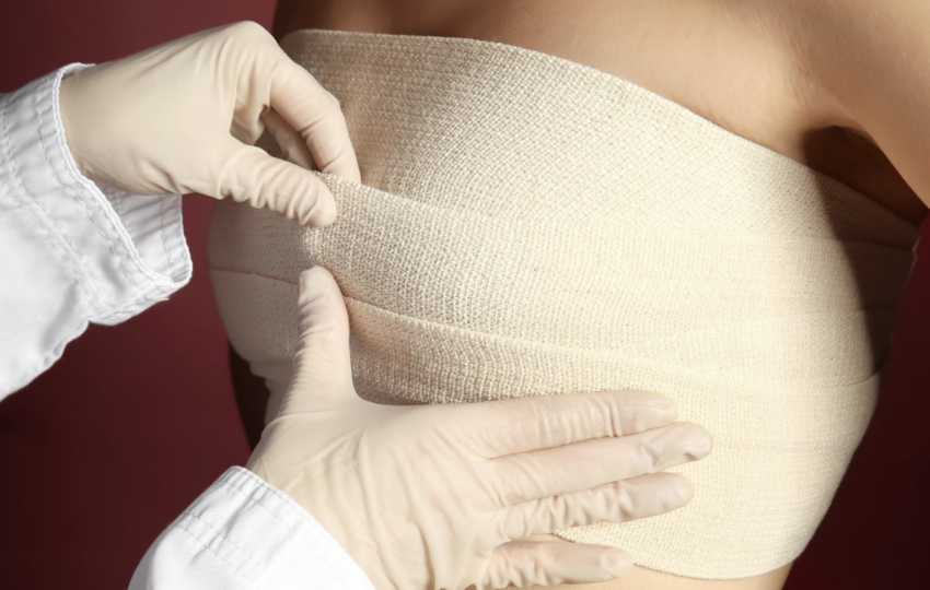 一名醫護人員戴著白色乳膠手套，正細心地為一名女性的胸部纏繞並調整彈性繃帶，呈現出整形手術後或醫療護理的術後加壓包紮過程。