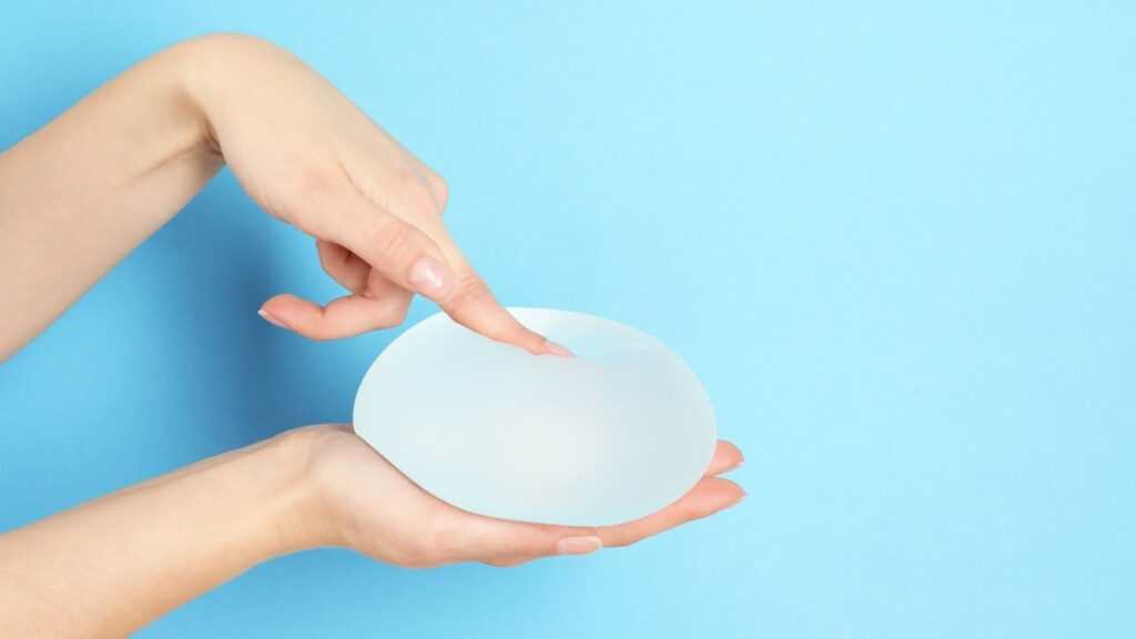  特寫鏡頭顯示一雙手輕輕觸碰並按壓一個半透明的矽膠乳房植入物，呈現材質的柔軟度與高彈性。