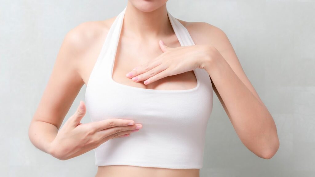 一名女性穿著白色運動內衣，雙手輕輕放在胸部上方與側面，展現自信的體態與手術後的視覺效果