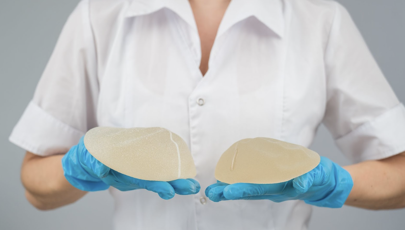 醫護人員戴著藍色乳膠手套，雙手各持一個不同尺寸的圓盤型矽膠隆乳植入物，展示醫學美容手術中使用的填充材質。