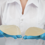醫護人員戴著藍色乳膠手套，雙手各持一個不同尺寸的圓盤型矽膠隆乳植入物，展示醫學美容手術中使用的填充材質。