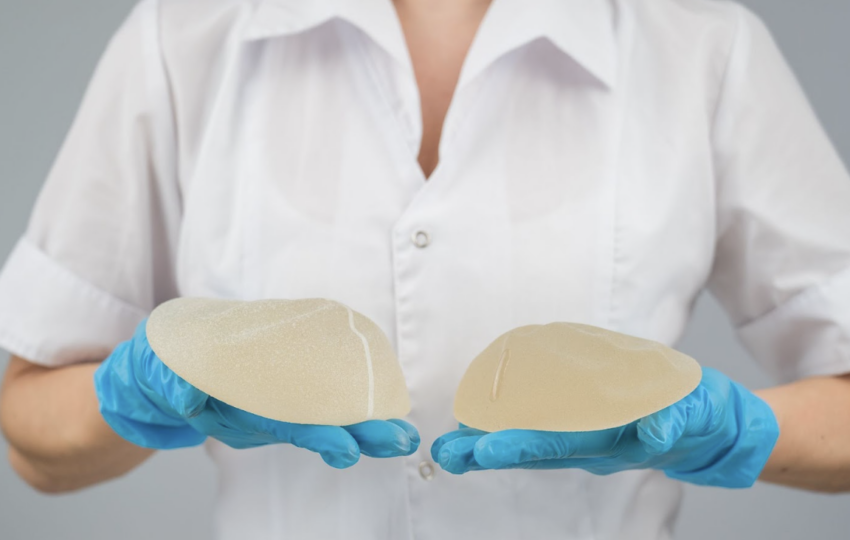 醫護人員戴著藍色乳膠手套，雙手各持一個不同尺寸的圓盤型矽膠隆乳植入物，展示醫學美容手術中使用的填充材質。