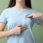 一名穿著淺藍色 T 恤的女性，使用雙手手指指向胸部特定位置，示意自我檢查或諮詢手術改善部位的情境