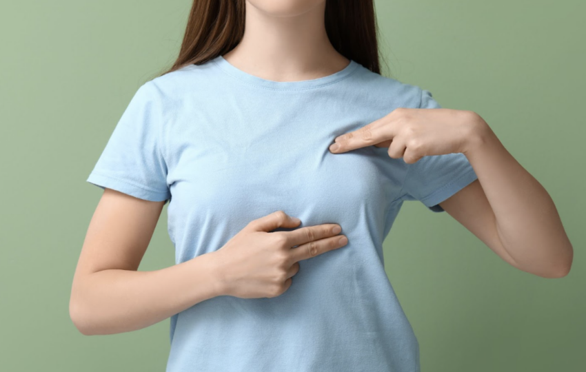 一名穿著淺藍色 T 恤的女性，使用雙手手指指向胸部特定位置，示意自我檢查或諮詢手術改善部位的情境